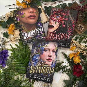 May include: Three hardcover books with floral face designs. The titles are "Belladonna", "Foxglove", and "Wisteria" by Adalyn Grace. The books are surrounded by dried flowers and greenery on a vintage paper background.