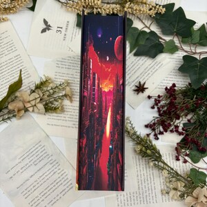 May include: A book with a vibrant, futuristic cityscape design on the spine. The artwork features tall buildings, a fiery sky, and celestial bodies in shades of red, orange, and purple. The book is surrounded by pages and floral accents.