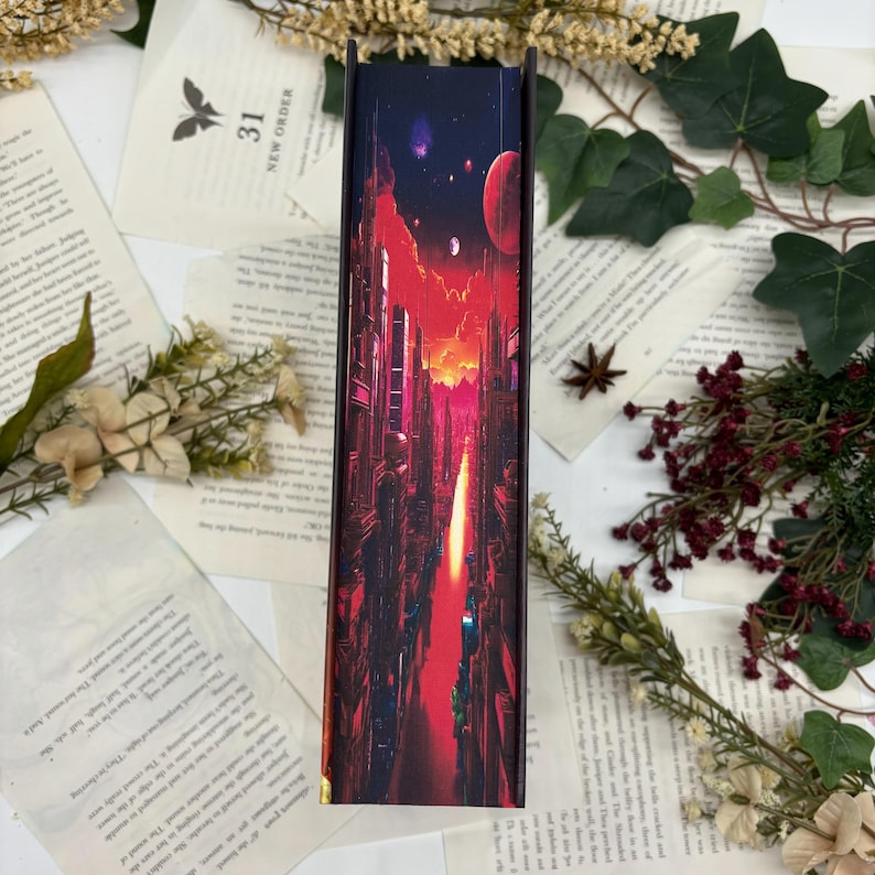 May include: A book with a vibrant, futuristic cityscape design on the spine. The artwork features tall buildings, a fiery sky, and celestial bodies in shades of red, orange, and purple. The book is surrounded by pages and floral accents.