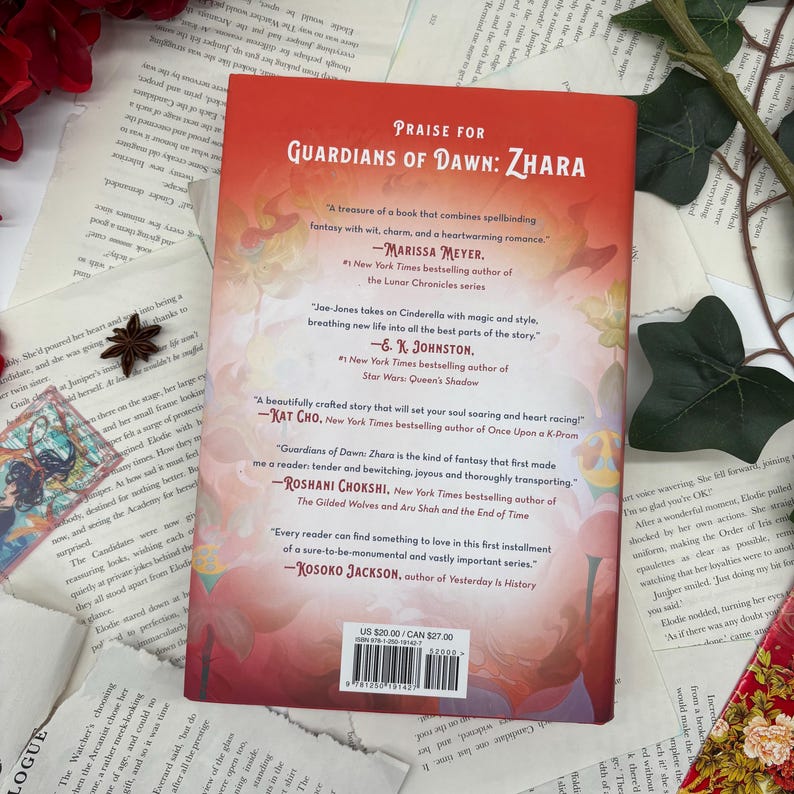 May include: Book cover for "Guardians of Dawn: Zhara" by Roshani Chokshi. The cover features a colorful illustration of a woman in a flowing dress with a crown on her head. The background is a vibrant sky with clouds and stars. The book is described as a fantasy novel with a heartwarming romance.