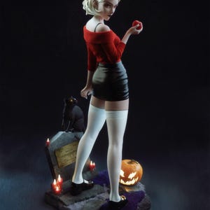 May include: A figurine of a woman in a red sweater, black skirt, and white thigh-high socks, holding an apple. A black cat sits on a tombstone, with a carved pumpkin and candles nearby. The figure has blonde hair and is wearing a black headband.