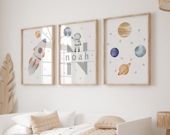 Puede incluir: Tres impresiones enmarcadas con temática espacial. La primera impresión presenta un cohete, la segunda impresión presenta un astronauta con el nombre "Noah" y la tercera impresión presenta planetas y estrellas.