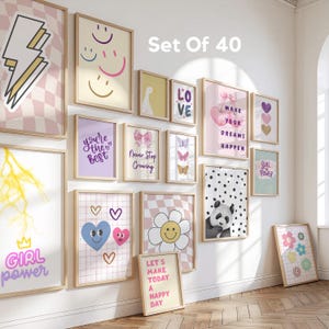 Op de afbeelding: Een verzameling van 40 ingelijste kunstprints met diverse ontwerpen, waaronder een bliksemschicht, smiley gezichten, harten, een madeliefje en een panda. De prints tonen positieve boodschappen zoals "Girl Power" en "Make Your Dreams Happen."