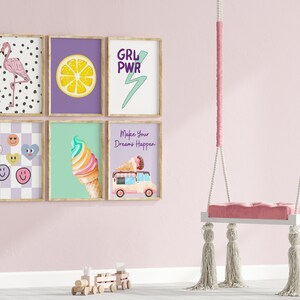May include: Five framed prints with various designs, including a flamingo, a lemon, a lightning bolt, ice cream, and a smiley face. The prints are hanging on a pink wall with a white swing hanging in front of them.