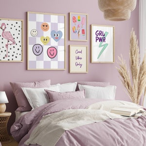 May include: A bedroom with a light purple wall and a bed with a light purple duvet and white pillows. There are several framed prints on the wall, including one with a flamingo, one with smiley faces, one with ice cream cones, and one with the text "GRL PWR" and a lightning bolt.
