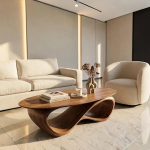 May include: A dark wood coffee table with a smooth oval top and a continuous, curved, sculptural base. The table holds two stacked books, a small white candle in a dish, and a beige ceramic vase containing dried botanical stems.