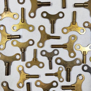 May include: A collection of antique brass clock winding keys. The keys have different sizes and shapes, with some having markings like "3.75" and "5.0".
