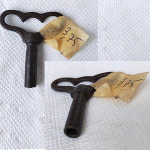 May include: A vintage clock key with a heart-shaped handle. The key is made of metal and has a dark brown finish. The key is labeled with the number "375".