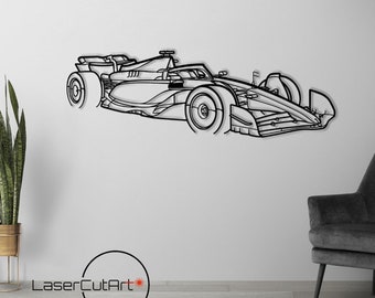 Op de afbeelding: Zwarte metalen wandkunst van een Formule 1-raceauto. Het kunstwerk is een gedetailleerde omtrek van het ontwerp van de auto, gemonteerd op een witte muur. De afbeelding bevat een zwarte stoel, een vloerlamp en een plant in een pot.