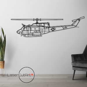Puede incluir: Una escultura de pared de metal negro de un helicóptero. El helicóptero está en vuelo y tiene una estrella en el lateral. La escultura está montada en una pared blanca.
