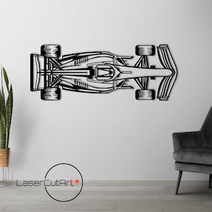 Puede incluir: Arte mural de metal negro de un coche de carreras de Fórmula 1. La obra muestra una vista superior del coche, destacando su diseño aerodinámico. Montada en una pared blanca, añade un toque moderno a cualquier espacio.