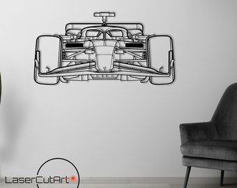 Op de afbeelding: Een zwart-witte lijntekening van een raceauto, gemonteerd op een witte muur. De auto is naar de kijker gericht en heeft een strak, modern ontwerp. De afbeelding is geplaatst tegen een witte muur met een zwarte fauteuil en een staande lamp op de achtergrond.