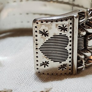 K&ouml;nnte beinhalten: Nahaufnahme eines silbernen Armreifs. Das Armband weist aufwendige Designs auf, darunter Sternmuster und Streifen. Der Verschluss ist mit dekorativen Elementen versehen. Das Gesamtdesign ist aufwendig und detailliert.