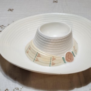May include: A white ceramic serving dish with a sombrero design. The dish has a wide, shallow brim with a ridged texture and a central, raised bowl. The sombrero's band is beige with green and brown accents.