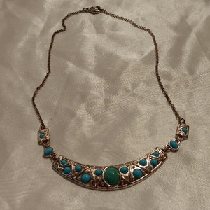 May include: A gold tone necklace with a turquoise and silver pendant. The pendant is shaped like a crescent moon and features a large turquoise stone in the center.
