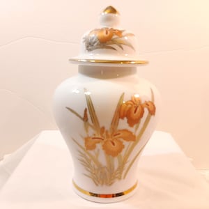 May include: White porcelain vase with a gold lid and a floral design of orange irises and gold leaves.