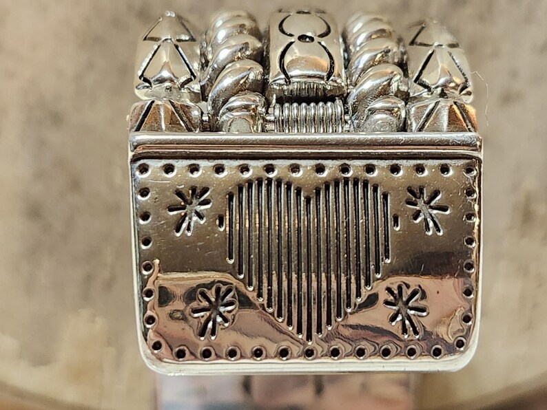 K&ouml;nnte beinhalten: Eine silberfarbene dekorative Metallbox mit herzf&ouml;rmigem Design und Schneeflocken-Akzenten. Die Oberseite zeigt stilisierte B&auml;ume und gedrehte, seilartige Elemente. Die Box hat eine rechteckige Form mit detaillierter, strukturierter Oberfl&auml;che.