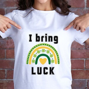 May include: White t-shirt with a green shamrock rainbow and the text "I bring luck" in black.