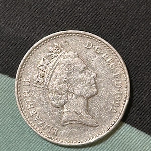 Puede incluir: Moneda de plata con un perfil de la reina Isabel II y el texto "D.G. REG. F.D. 1993" en el anverso.