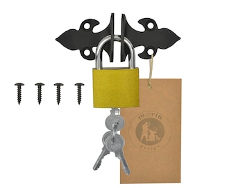 May include: A black metal latch with a gold padlock and two keys. The latch is attached to a wall with screws. The padlock has a brown paper tag with the text "moria design" and a logo of two people dancing.