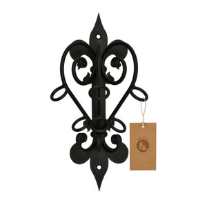 Puede incluir: Estante de vino de pared de metal negro con un diseño decorativo en forma de corazón y una base de flor de lis. El estante tiene cuatro ganchos para colgar copas de vino.