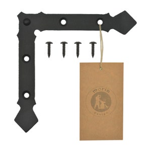 Può includere: Angolo in metallo nero con un design decorativo. Viene fornito con quattro viti nere e un'etichetta di carta marrone con il testo "moria design".