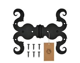 May include: Black metal decorative hinge with a scroll design. The hinge is attached to a brown paper tag with the text "moria design" printed on it. The hinge comes with six black screws.