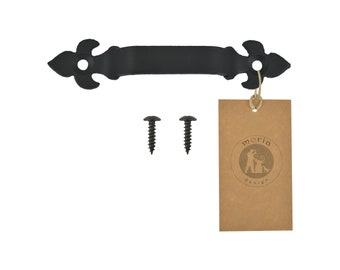 May include: Black metal door pull with a fleur-de-lis design. The pull comes with two black screws. The pull has a brown paper tag with the text "moria design" in black.