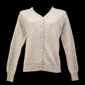Könnte beinhalten: Hellgraue Strickjacke mit V-Ausschnitt und langen Ärmeln. Der Pullover hat einen gerippten Saum und Bündchen und wird mit sechs runden, weißen Knöpfen vorne geschlossen. Der Hintergrund ist einfarbig schwarz.