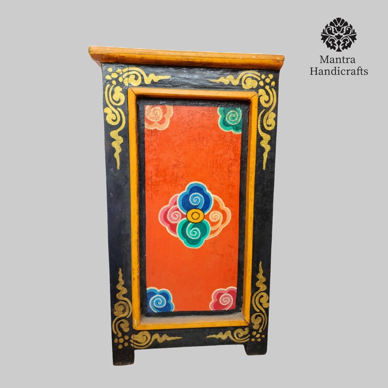 May include: A small, black wooden cabinet with a red, orange, blue, and green painted design. The cabinet has a yellow trim and gold accents.