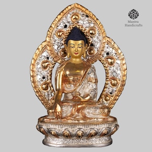 May include: A gold and silver Buddha statue seated in a meditative pose. The statue is decorated with intricate details and sits on a throne with a heart-shaped back.