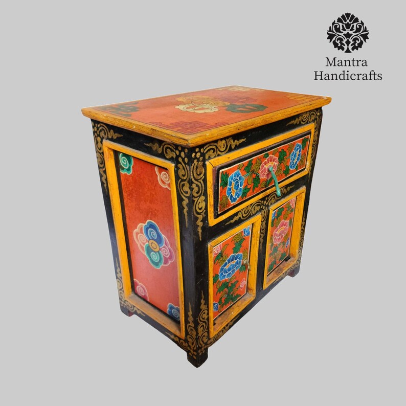 May include: A small, hand-painted wooden cabinet with a drawer and two doors. The cabinet is decorated with colourful floral designs and gold accents. The cabinet is black with red, yellow, blue, and green paint.
