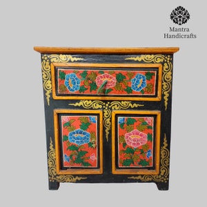 May include: A black wooden cabinet with two doors and a drawer. The cabinet is decorated with intricate floral designs in shades of red, blue, green, and gold. The cabinet is a traditional Tibetan style.