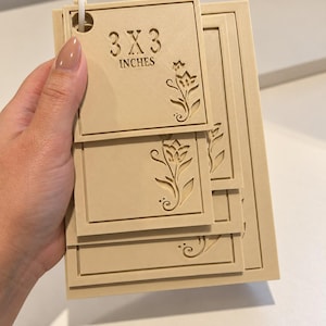 May include: A set of beige rectangular plastic tags held together by a white ring. The top tag features the text 3 X 3 INCHES and a floral cutout design. Each tag has a raised border and a matching floral cutout motif on the right side.