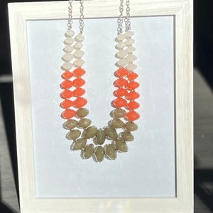 May include: A multi-strand necklace with graduated beads in shades of white, orange, and green. The beads are faceted and have a slightly irregular shape.