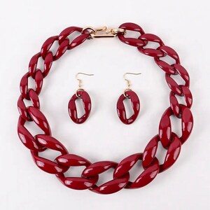 May include: A set of red chunky chain necklace and earrings. The necklace is made of large, thick, red plastic links. The earrings are also made of red plastic and are shaped like ovals.