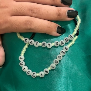 May include: Two beaded bracelets with black and white beads. The top bracelet spells "SAY MY NAME" and the bottom bracelet spells "JUICE IS LOOSE".