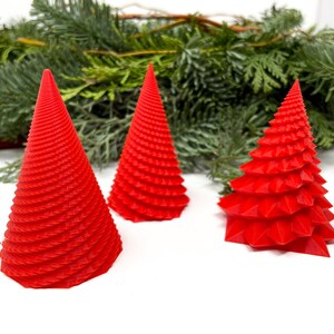 May include: Three red Christmas tree ornaments, two are cone shaped with a spiral design and one is a more traditional tree shape.