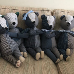May include: Five patchwork teddy bears in blue and grey plaid fabric sitting on a beige sofa. The bears have black eyes and noses and are all wearing blue and white ribbon bows.
