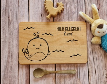 May include: A wooden cutting board with a whale design and the text "HIER KLECKERT Levi" engraved on it. The board is surrounded by wooden toys, including a rooster and a bunny.