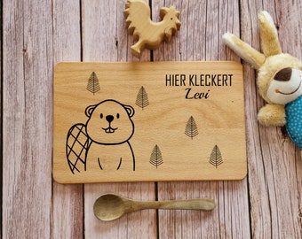 May include: A wooden plate with a beaver illustration and the text "HIER KLECKERT Levi" in black lettering. The plate is surrounded by a wooden surface and a wooden spoon.