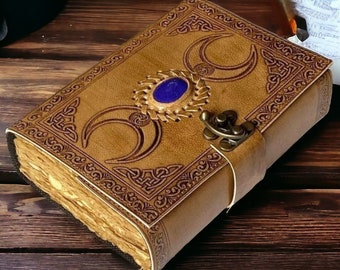 May include: A brown leather journal with a decorative clasp and a blue gemstone. The cover features three crescent moons and intricate Celtic knotwork.
