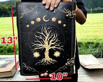 Puede incluir: Un diario de cuero negro con un diseño de árbol dorado y fases lunares. El diario mide 13 pulgadas de alto y 10 pulgadas de ancho.