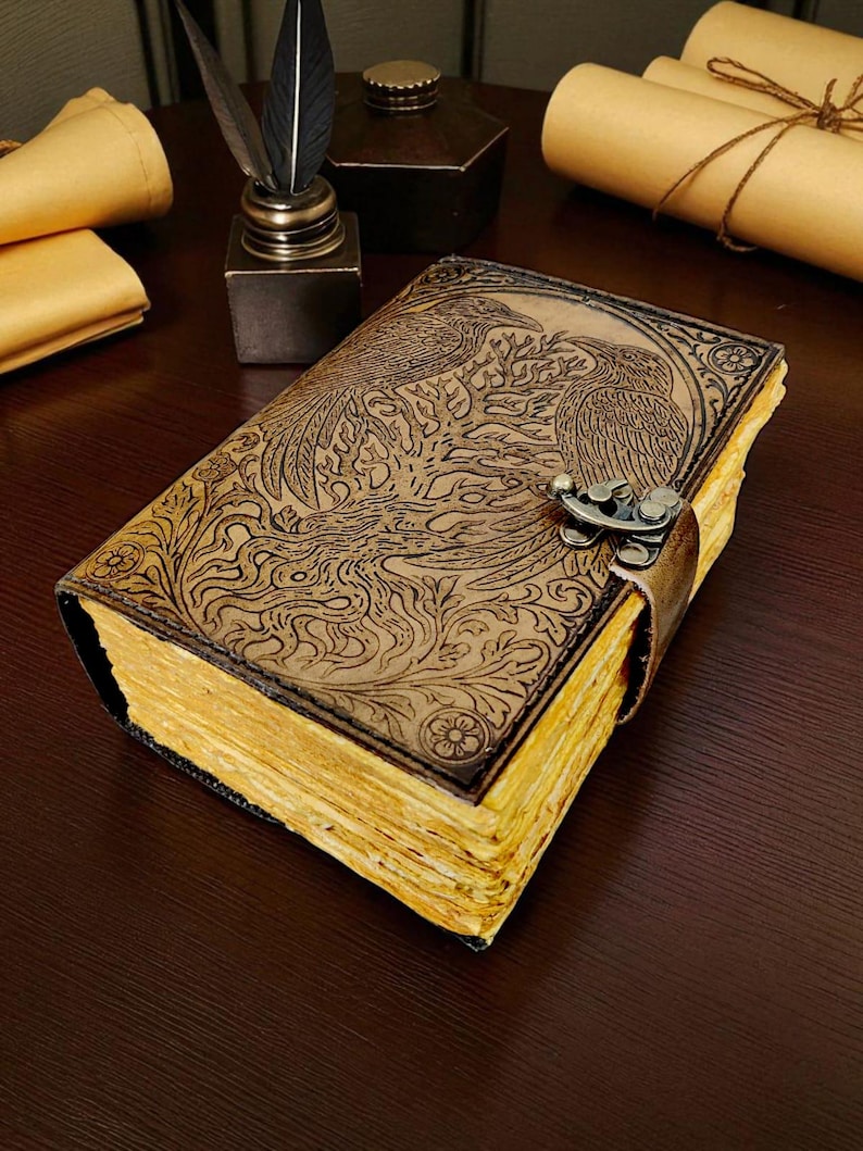 May include: A brown leather journal with an embossed design of two birds and foliage. The journal has a metal clasp and a leather strap closure. The pages have a yellowed, aged appearance. The journal is on a dark wooden surface.