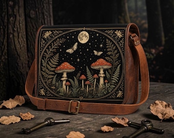 Könnte beinhalten: Eine rechteckige braune Ledertasche mit einer schwarzen Frontplatte, die eine detaillierte Illustration von roten Pilzen, Farnen, Schmetterlingen und einem Vollmond vor einem Sternenhimmel zeigt, inklusive verstellbarem Schulterriemen und Metallschnalle.