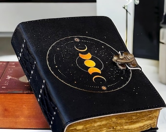 May include: Black leather journal with a gold moon phases design and a brass clasp. The journal has a distressed look and a textured cover.