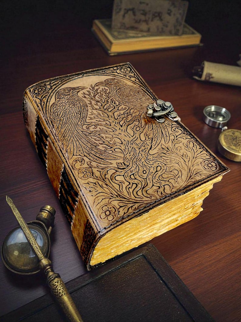 May include: A leather-bound journal with an embossed design of two birds and floral patterns. The journal has a metal clasp and aged, yellowed pages. The cover is a light brown color, and the edges of the pages are gilded.