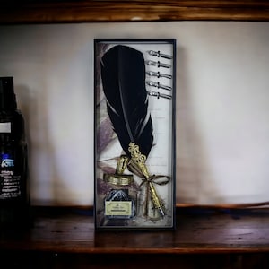 Op de afbeelding: Een vintage kalligrafieset met een grote zwarte veerkiel met een goudkleurige metalen penpunt en decoratieve accenten. De set bevat een kleine inktfles en verschillende penpunten, allemaal gepresenteerd in een rechthoekige doos.