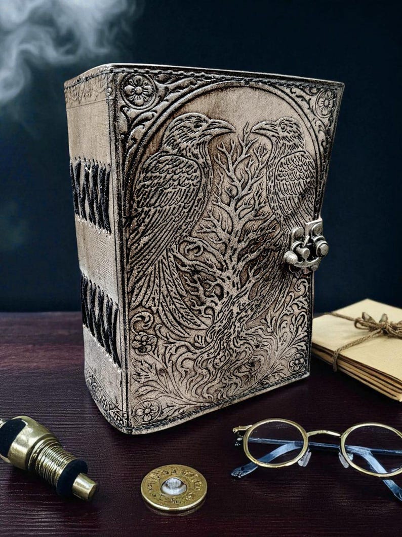 Puede incluir: Un diario de cuero beige con un dise&ntilde;o en relieve detallado con dos cuervos y un &aacute;rbol. El diario tiene un cierre de metal y patrones florales. El lomo tiene costuras negras. Un art&iacute;culo &uacute;nico, hecho a mano.