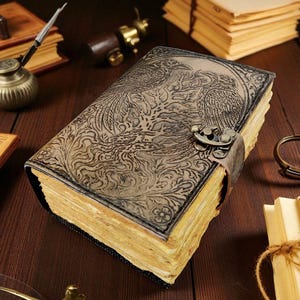 Puede incluir: Un diario encuadernado en cuero con un dise&ntilde;o de f&eacute;nix en relieve. El diario tiene un cierre de metal y una correa de cuero. Las p&aacute;ginas est&aacute;n envejecidas y la cubierta es de color marr&oacute;n oscuro. Sobre una superficie de madera.